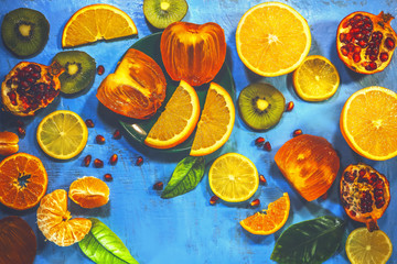 sliced ​​citrus fruits on a blue painted board. orange, kiwi, pomegranate, persimmon, mandarin.