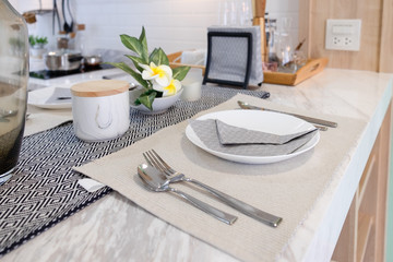 Set of modern dining table with white plate, spoon and fork near flower on marble table. Interior design for decoration home.