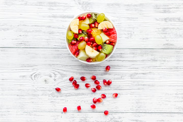 Fruit diet concept. Fruit salad with apple, kiwi and pomegranate in bowl on white wooden background top view copy space