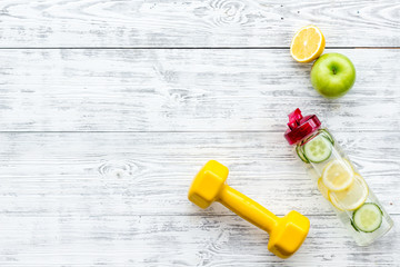 Fototapeta na wymiar Healthy fruit water for sport, fitness. Bottle of water with lemon and cucumber near sport equipment dumbbells on white wooden background top view copy space