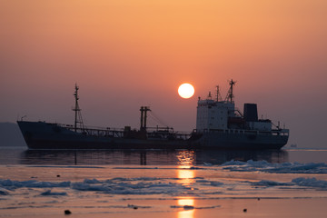 Fototapeta premium The silhouette of the ship against the sea and a bright sunset.