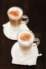 Coffee in glass on the wooden background.  A glass with cappuccino and cinnamon. 