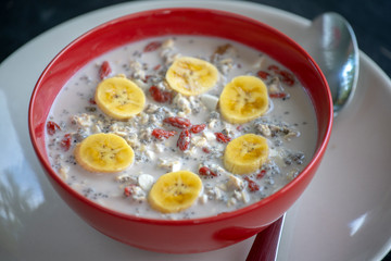 Fresh breakfast of granola, yogurt, nuts, goji berries, chia seeds and banana. Muesli with fruits and berries in red bowl