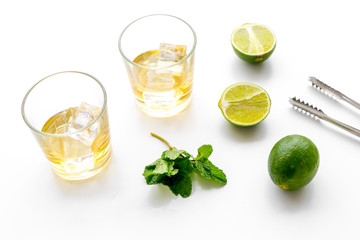 Copmosition with whiskey. Iced whiskey near mint, lime, bar tongs on white background top view