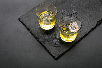 In the bar. Whiskey with ice on black desk on black background top view copy space
