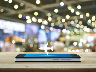 Airplane flat icon on modern smart mobile phone screen on wooden table over blur light and shadow of shopping mall, Business transportation online concept