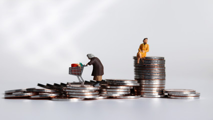 A miniature woman pulling a cart from a pile of coins and a miniature woman sitting on a pile of...