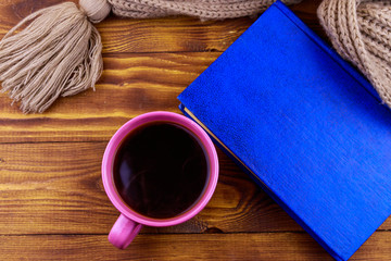 Cup of coffee, knitted scarf and book on wooden background