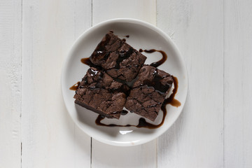 A plate of brownies with chocolate sauce on white wooden background, mint leaf on top, top view