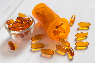 Vitamin D from Fish oil capsules in an orange bottle on white wooden background, supplemental and healthcare product, alphabet cube arranged in words