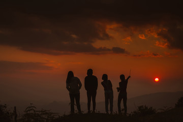 The silhouette of a woman standing watching the sunset sky Darling pointed to the cloud Colorful sky, orange sky and golden sky Queue of close friends