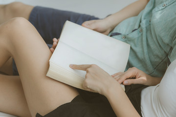 White cozy bed and a beautiful young loving couple bonding to each other, reading a book while sitting on bed, concepts of home and comfort, place for text.