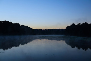 Early foggy Morning over a dark Pond with a Reflection of the forest in the water. Sunrise over small lake