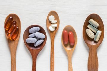 Variety of vitamin pills in wooden spoon on white background, supplemental and healthcare product, flat lay surface