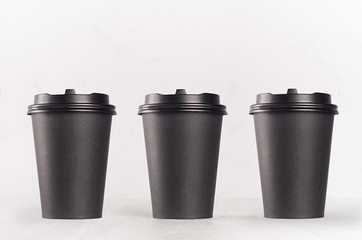 Coffee mockup - set of three blank black paper cups with cap on white wood table, coffee shop...