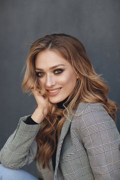Portrait of beautiful woman with long curly blond hair outdoors in spring. Young woman with natural makeup in a gray jacket . A smart photo of a young beautiful woman in autumn clothes.