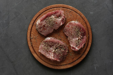 Three raw stakes with rosemary on round board
