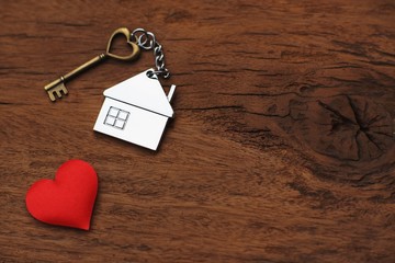 House key with home keyring decorated with mini red heart on wood texture background, sweet home concept