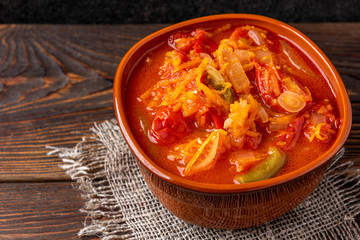 Homemade pickled salad of tomato, pepper, onion and carrot on dark wooden background.