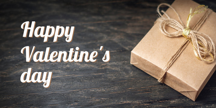 Holiday box Packed in crafting paper on dark wooden background. Holiday horizontal card Happy Valentine's day with text