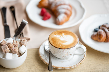 Coffee cappuccino with two croissant on white plate in restaurant. Light morning Breakfast, fresh warm pastries and raspberries