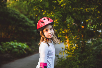 Little girl rides on rollers in summer park. Girl look in camera and smile. Child wearing...