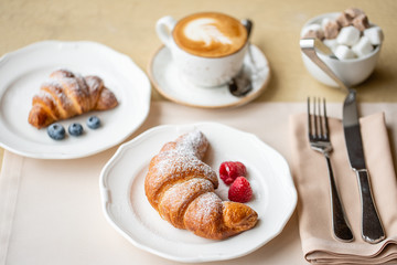 Coffee cappuccino with two croissant on white plate in restaurant. Light morning Breakfast, fresh warm pastries and raspberries