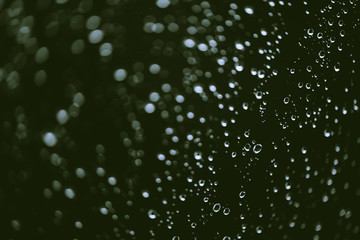 Dirty window glass with drops of rain. Atmospheric green background with raindrops in bokeh. Droplets and stains close up. Detailed transparent texture in macro with copy space. Rainy weather.