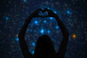 Silhouette of a girl holding heart-shape symbol for love on a starry night sky. My astronomy work.