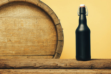 Black beer bottle on a old wooden table. Barrel background.