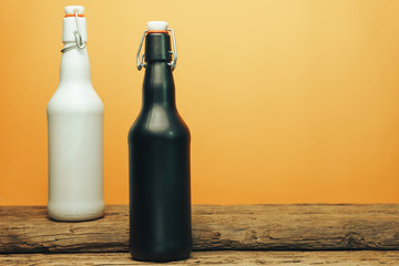 Black and white beer bottle on a old wooden table. Yellow background.