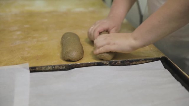Close up for baker hands preparing raw rye for the loaf, food concept. Woman hands making a baguette from the raw rye dough onwooden board at the bakery.