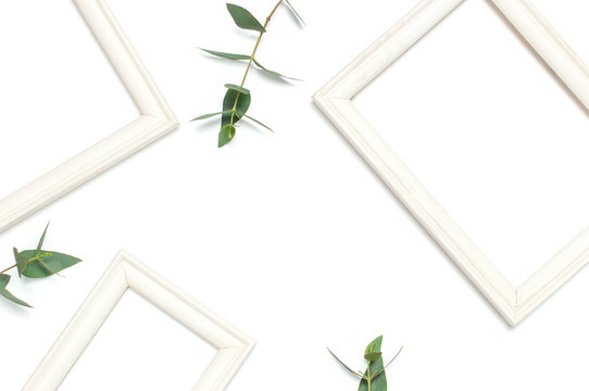 White wooden photo frame and green eucalyptus leaves on white background. Flat lay top view copy space. Stylish minimal composition, artwork mockup, picture frame, home decoration