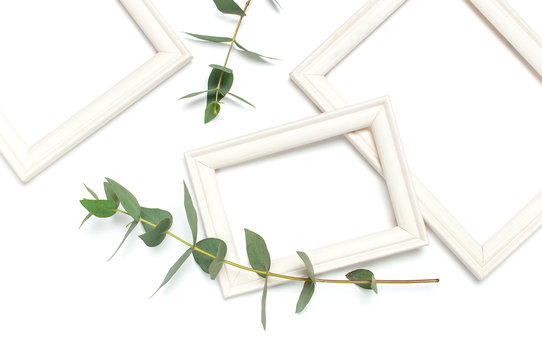 White wooden photo frame and green eucalyptus leaves on white background. Flat lay top view copy space. Stylish minimal composition, artwork mockup, picture frame, home decoration