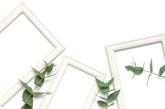 White wooden photo frame and green eucalyptus leaves on white background. Flat lay top view copy space. Stylish minimal composition, artwork mockup, picture frame, home decoration