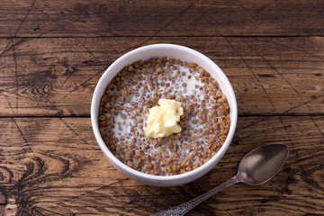 Homemade delicious healthy breakfast. Buckwheat porridge with milk and butter on a wooden table, horizontal