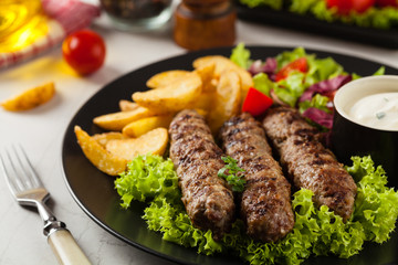 Traditional cevapcici served with baked potatoes. Stone background.