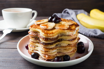 Pancake cake with bananas and berry syrup, selective focus, dark background.