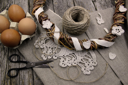 Easter composition on wooden background. Preparation for the holiday. Handmade crochet lace, homemade chicken egg, natural wreath from vine branches, linen fabric. Cozy rustic, country style.