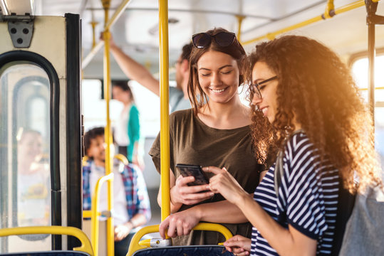 Two Friends Looking In Phone While Standing On A Bus.