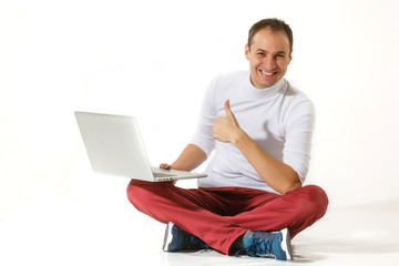 Happy young man sitting on a floor and using laptop isolated over white background