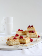 Sliced crumble pie with raspberries on top on a marble plate and cups in the background