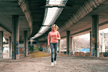 Gorgeous blonde woman wearing sportswear and with ponytail running under the bridge.