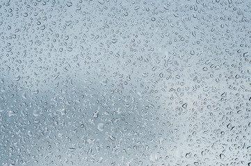 closeup of rain drops on window on cloudy sky background