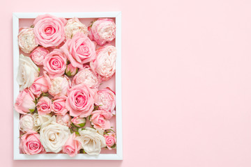 Festive floral design. Mothers day congratulation. Pink roses arranged in white frame. Copy space on pink background.