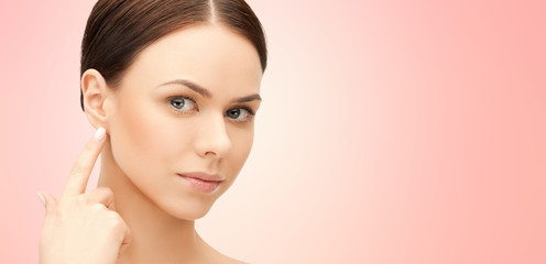 Fototapeta premium beauty, hearing and plastic surgery concept - face of beautiful young woman pointing finger to earlobe over pink background