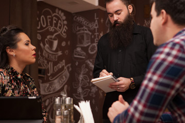 Waiter taking order from stylish couple in restaurant Hipster restaurant.