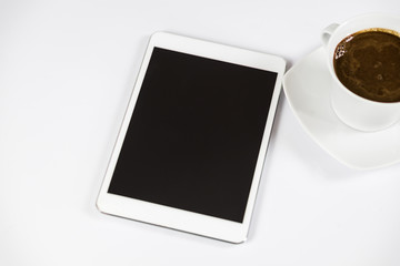 Computer tablet with empty screen next to coffee. The tablet is on the white table. View from the top. Close-up.