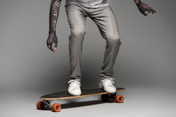 low section of stylish tattooed man balancing on skateboard on grey