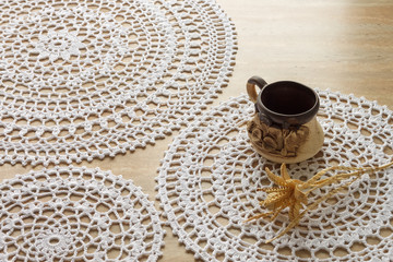 Crocheted round-type napkins of white color, a cup of coffee and the flower is made of straw